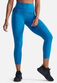 Höga blå leggings i ett smidigt, stretchy material, med en åtsittande design och kort längd, kombinerade med svarta träningsskor.