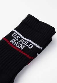 Calzini neri a coste con strisce bianche e rosse e logo "U.S. POLO ASSN" in testo bianco. Materiale in misto cotone con una consistenza morbida.