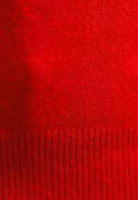 Tessuto lavorato a maglia rosso con una consistenza morbida e pelosa e un motivo a coste nella parte inferiore. Uniformità di colore uniforme in tutto il tessuto.