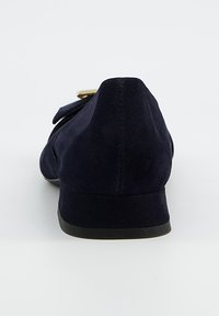 Chaussure plate en daim bleu marine avec un bout arrondi et une petite semelle en caoutchouc noire. Elle présente un nœud décoratif et un détail en métal doré.