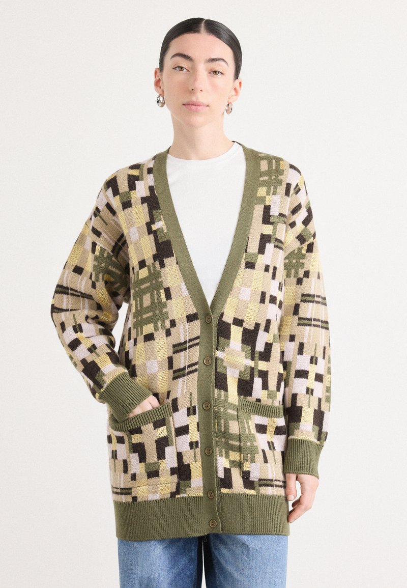 Adīta džemperis ar ģeometrisku rakstu olīvu, beigu un brūnā krāsā. Iezīmējies ar dziļu V-veida kaklu, pogām un divām priekšējām kabatām. Ribotas aproces un apakšdaļa.