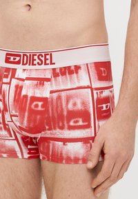 Boxer rossi in cotone con un elastico bianco in vita con la scritta 'DIESEL' in rosso. Il tessuto presenta un motivo grafico audace con tonalità di rosso sfumate.