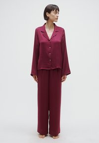 Ensemble pyjama bordeaux deux pièces composé d'une chemise à manches longues à boutons et d'un pantalon ample, fabriqué en tissu lisse avec un léger éclat.