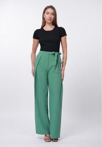 Črna prstanasta majica s kratkimi rokavi, kombinirana z visokim pasom, širokimi zelenimi hlačami, ki imajo pas s trakom in gladko tkanino.