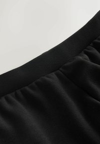 Nahaufnahme eines schwarzen Stoffes mit glatter, weicher Textur und einem elastischen Bund, der gerafftes Material für zusätzlichen Komfort zeigt.