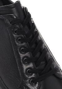 Sneaker in pelle nera con superficie testurizzata, lacci neri rotondi, occhielli metallici e un design elegante con punta liscia.
