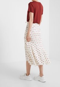 Gonna bianca con pois rossi, design a campana. Abbinata a una camicia a maniche corte borgogna e sneakers bianche. Tessuto con una texture liscia.