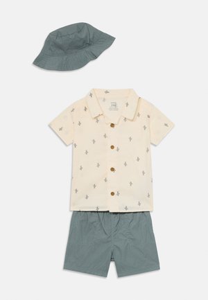 Camisa de botão de manga curta em creme com estampa de cactos, combinada com calções teal e um chapéu de balde a condizer. O tecido é uma mistura leve de algodão.