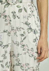 Bloemenpatroon broek met een lichte achtergrond, met groene bladeren en roze bloemen, gestructureerd ontwerp en verticale strepen.