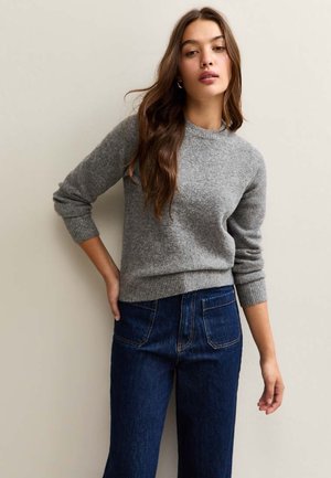 Pull en laine gris avec un col rond, des poignets et un ourlet côtelés. Associé à un jean taille haute en denim bleu foncé avec des poches arrière.