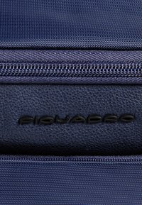 Marineblauwe stoffen tas met een gestructureerd lederen accent. Voorzien van een stevige ritssluiting en een gegraveerd logo. Gladde oppervlakte met fijne stikdetails.