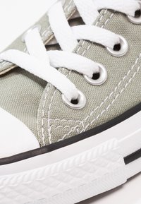 Hellgrünes Canvas-Sneaker mit weißen Schnürsenkeln, silbernen Ösen und einer weißen Gummikappe. Verfügt über eine strukturierte weiße Sohle mit schwarzen Akzenten.