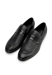 Mocasines de cuero negro con una textura de espiga y una banda suave en la parte superior. Diseño elegante, con punta redondeada y suela plana.