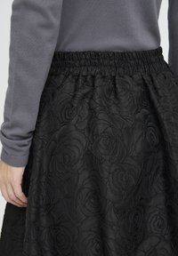 Black skirt featuring embossed rose pattern, elastic waistband, and textured fabric. Complimented by a gray long-sleeve top.