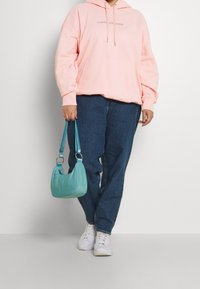 Sudadera con capucha rosa y logo, jeans de mezclilla azules, zapatillas blancas y un bolso azul claro con una correa trenzada.