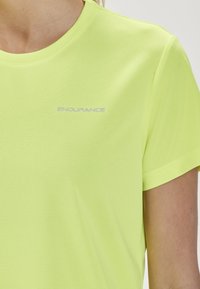 Kortärmad, fukttransportande skjorta i klar neon-gul med en texturerad yta. Har "ENDURANCE"-logotypen i subtil grå.