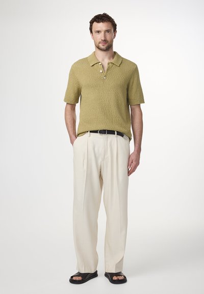 Olijfgroen gebreide polo met korte mouwen, drie knopen bij de hals, gecombineerd met crèmekleurige geplooide broek en zwarte sandalen. Zachte stoftextuur.