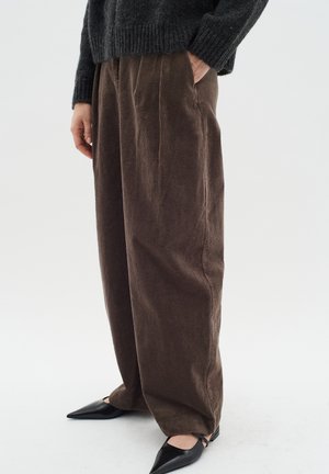 Brown corduroy trousers with a wide-leg design, featuring front pleats and side pockets. Paired with black pointed shoes.