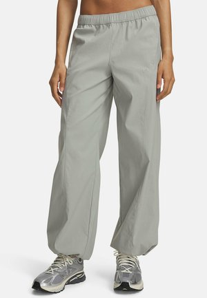 Person wearing light gray loose-fit pants with elastic waist and silver athletic shoes standing on a white background.