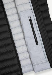 Chaqueta acolchada en blanco y negro abierta para mostrar el bolsillo interior con cremallera vertical negra en el forro blanco.