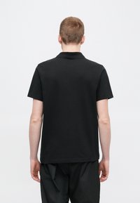 Must polo särk, lühikeste varrukatega, tehtud siledast puuvillast, klassikalise krae ja sirge äärega. Ilma nähtava brändingu või mustriteta.