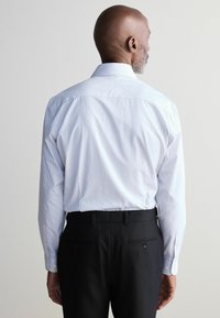 Chemise à manches longues pour hommes en bleu clair avec de fines rayures blanches, dotée d'un col boutonné et d'une coupe décontractée ; associée à un pantalon noir.