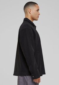 Black fleece jacket with a collar, side pockets, and buttoned cuffs. Features a relaxed fit and smooth texture, designed for comfort.