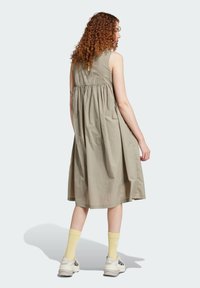 Kaki ärmlös klänning med en draperad midja och en flott A-linjeform, kombinerad med gula strumpor och vita sneakers.