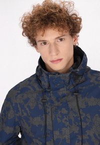 Giacca blu con motivo esagonale, dotata di cordini regolabili e colletto alto per protezione dalle intemperie. Tessuto con una texture liscia.