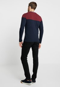 Pitkähihainen paita, jossa on tummansininen vartalo ja viininpunainen yläosa. Yhdistetty mustiin housuihin ja tummansinisiin kenkiin, luoden rentoa ilmettä.