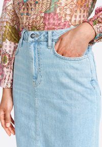 Gonna di jeans blu chiaro con vita alta, tasche frontali e dettagli di cucitura sottili. Abbinata a una blusa a maniche lunghe con motivo floreale.