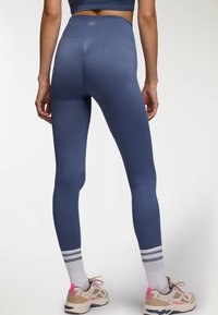 Niebieskie legginsy z wysokim stanem, z teksturowanym wzorem i wzmocnionymi szwami. W połączeniu z lekkimi sneakersami z różowymi akcentami i paskowanymi skarpetkami.