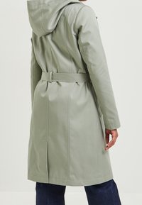 Svetle zelený kabát s kapucí a páskem v pase, hladká textura a dlouhé rukávy. Obsahuje švy a má délku po kolena.