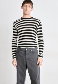 Chemise rayée noire et crème à manches longues associée à un pantalon en denim gris. La chemise a un col rond et des manches ajustées.
