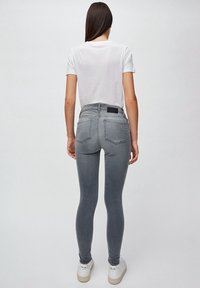 Vaqueros skinny grises con cintura alta, textura de denim, bolsillos traseros y etiqueta negra. Combinados con una camiseta blanca básica y zapatillas blancas.