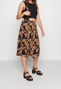 Svart blommig kjol med rosa och gula blommor, plisserad design, bärs med en figurnära svart crop top och kraftiga svarta plattformssandaler.