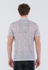 Kortærmet polo-shirt i lys grå med tekstureret stof. Har en stående krave og et subtilt mønster. Bæret med mørke jeans.