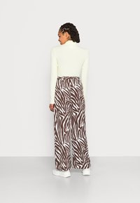 Top de manga longa, amarelo claro, combinado com calças largas em padrão zebra castanho e branco; modelo usa ténis brancos.