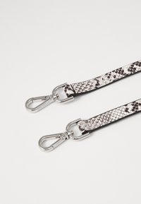 Sort-hvidt snogemønstret tekstureret rem med sølvfarvede metalklemmer i hver ende, lavet af syntetisk materiale.