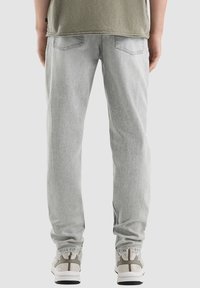 Lichtgrijze denim jeans met een relaxed fit, voorzien van achterzakken en opgerolde broekspijpen, gecombineerd met gedempte grijze sneakers.