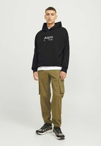 Zwarte hoodie met wit logo, khaki cargobroek met zakken en zwarte sportschoenen met grijze accenten. Eenvoudig, casual ontwerp.