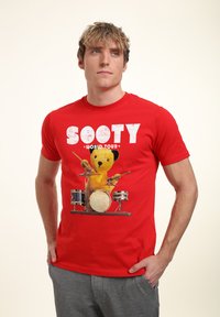 Červené bavlněné tričko s grafikou žlutého medvěda bubeníka a nápisem "SOOTY WORLD TOUR" v bílé, opotřebované fontu.