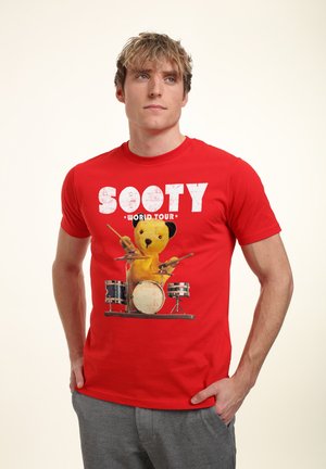 Červené bavlněné tričko s grafikou žlutého medvěda bubeníka a nápisem "SOOTY WORLD TOUR" v bílé, opotřebované fontu.