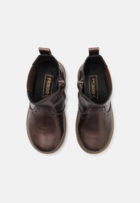 Botas de tobillo de cuero marrón con detalles de costura y cremalleras laterales, que presentan una superficie texturizada y una suela de goma marrón claro en contraste.