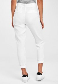 Pantalons en lin blancs avec une coupe décontractée, dotés de poignets retroussés et de poches arrière discrètes. Associés à des baskets noires et blanches.