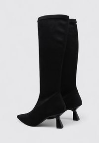 Botas negras hasta la rodilla con punta afilada, fabricadas en un material suave, con un diseño de tacón de reloj de arena único. Silueta simple y sin costuras.