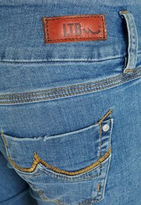 Jeans de ganga azuis com um rótulo de couro castanho com "LTB." O design inclui costuras decorativas no bolso de trás.