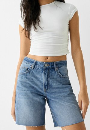 Shorts en denim bleu clair avec un ourlet brut et des poches cousues, associés à un haut ajusté à manches courtes blanc.