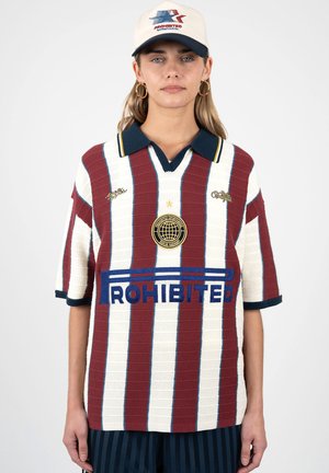 Ung kvinde iført en rød- og hvidstribet striktrøje med "Forbudt"-logo og en beige hat med et blåt og rødt emblem.