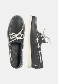 Zapatos de barco de cuero negro con costuras blancas. Presentan un diseño de cordones, suela de goma y cordones grises. Ligeros y con una textura suave.